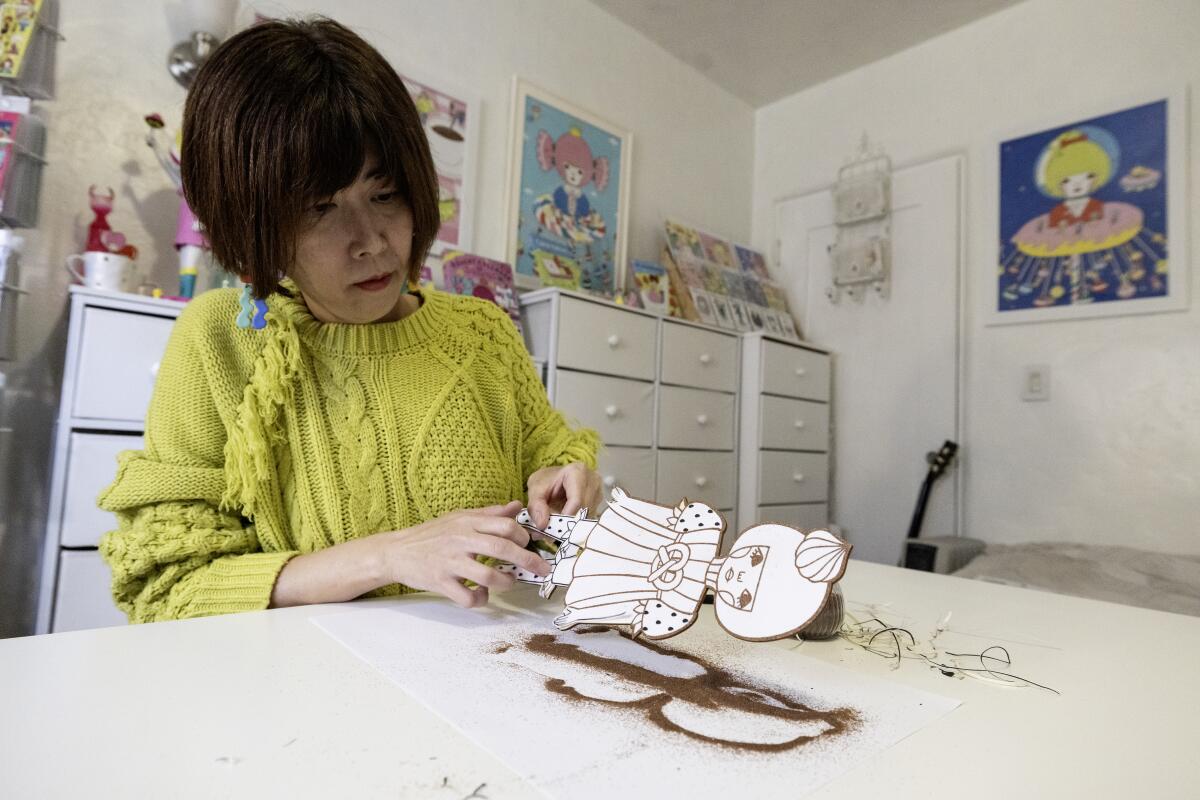 A woman holds a flat doll on a table.