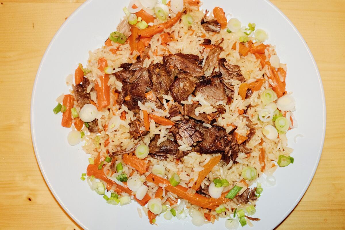 Rice pilaf made with beef, carrots, roasted garlic and chickpeas on a white plate on a wood table