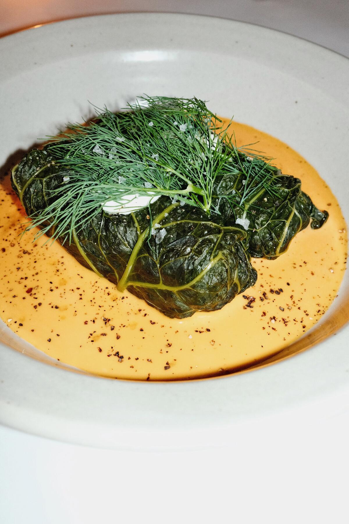 A bowl of two stuffed cabbage rolls with abalone rice atop  an orange-colored sauce at Little Fish in Melrose Hill.