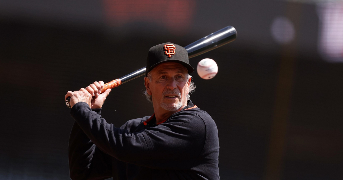 A man wearing a San Francisco Giants cap and black shirt is holding a baseball bat, preparing to hit a ball approaching him.