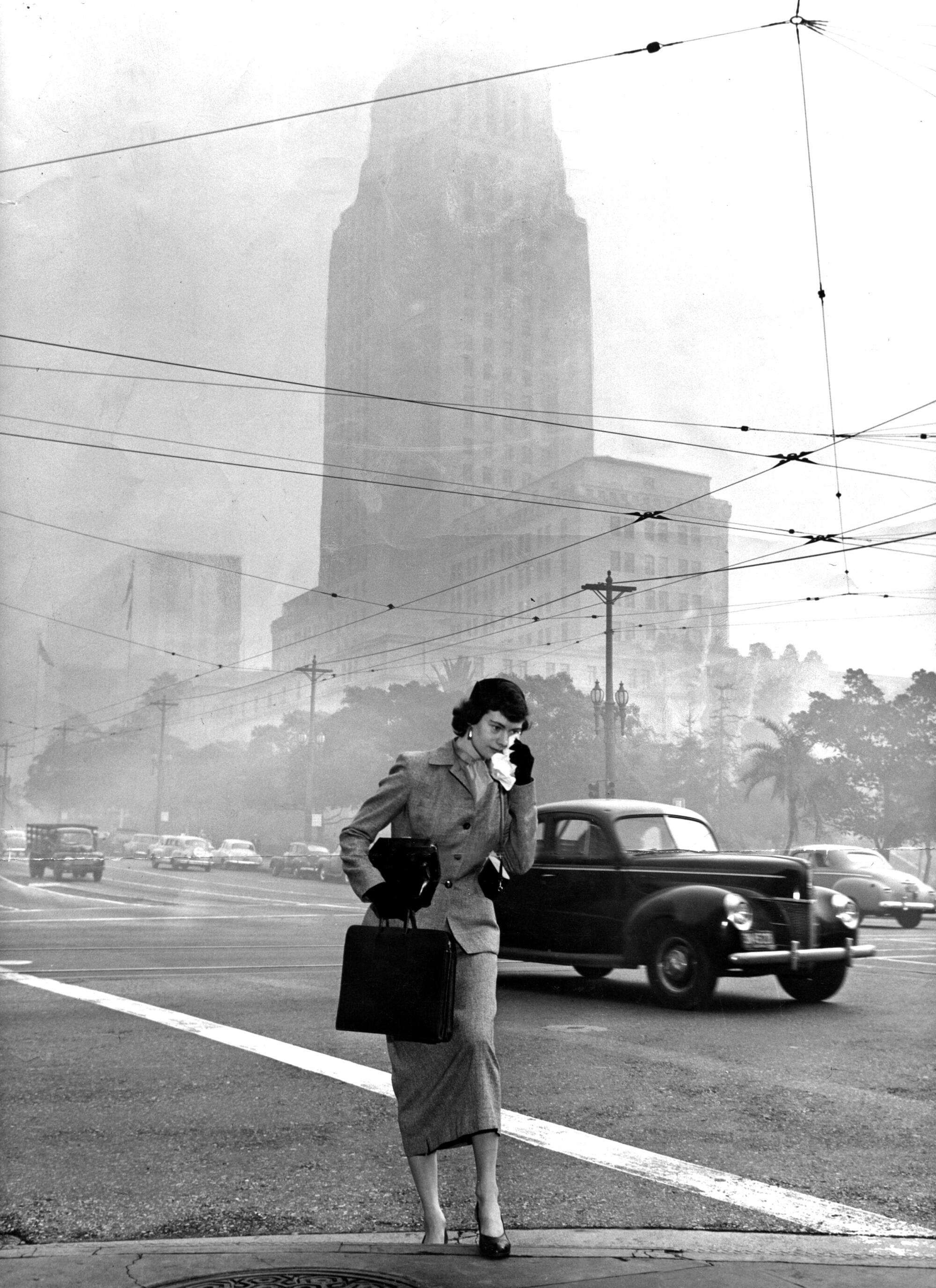A woman walks to work in smog-filled downtown L.A. in February 1953, with City Hall in the background.
