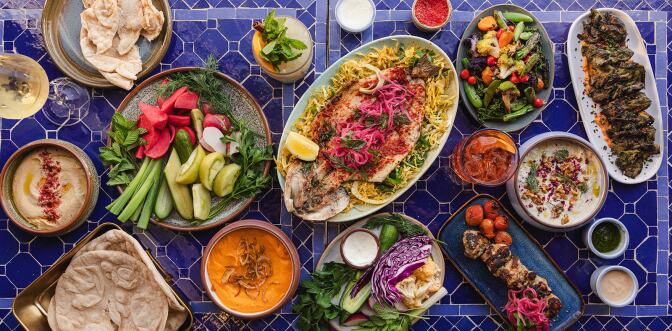 An assortment of Middle Eastern food on a table, including grilled fish, pita, pickled vegetables and dips. 
