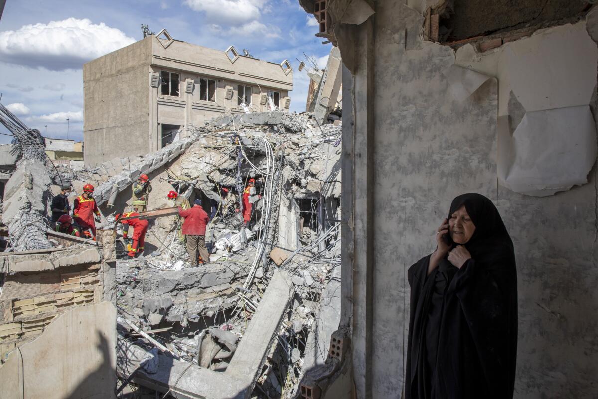 A woman speaks on the phone as emergency workers sift through rubble of a residential building that was hit in an airstrike.