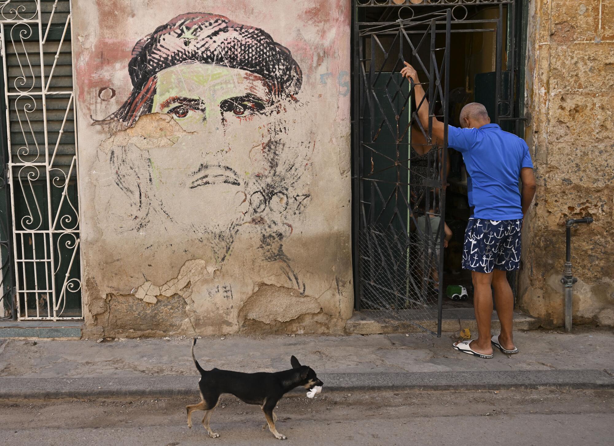 A man enters his home next to a fading mural of Che Guevara