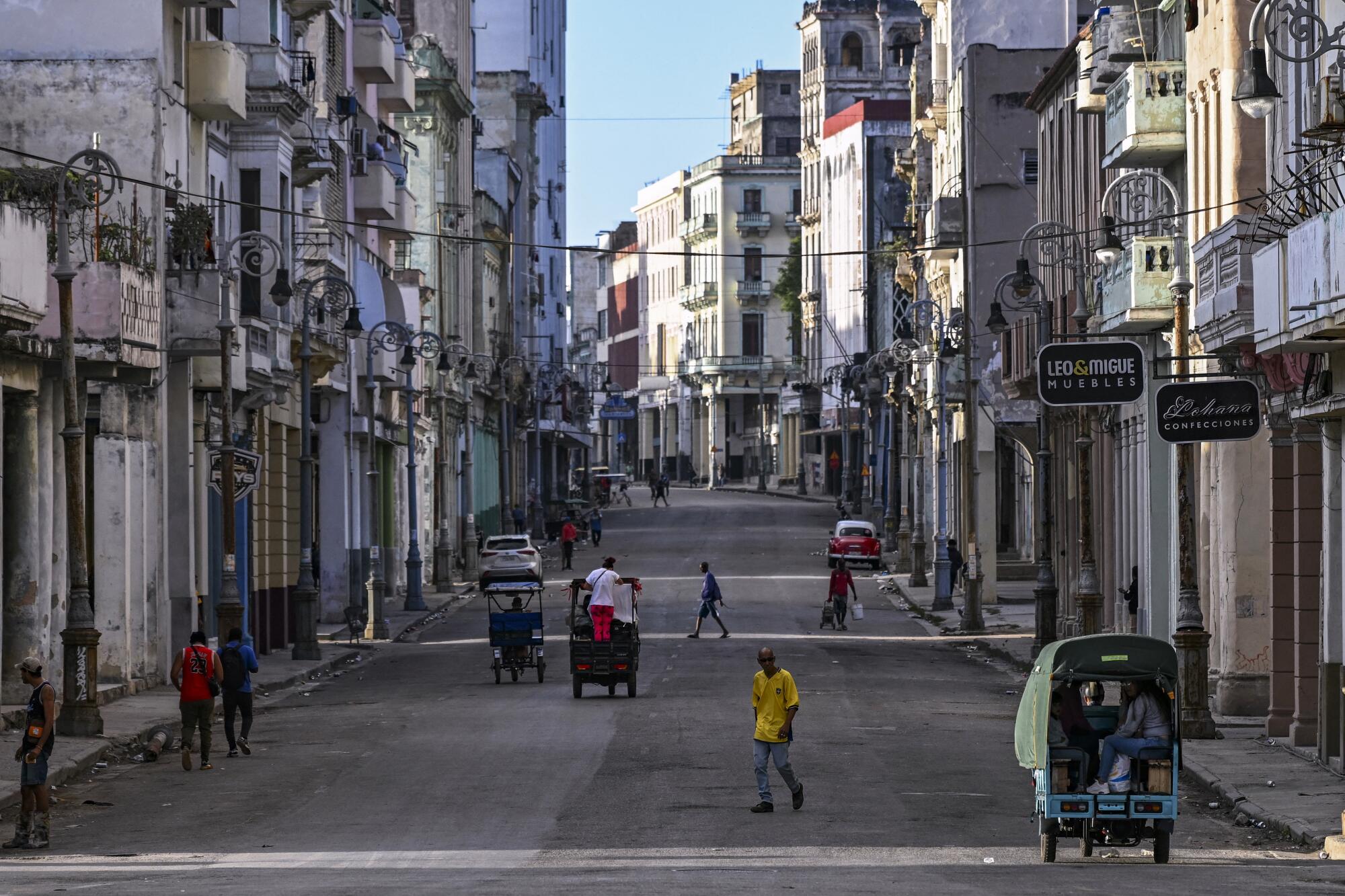 People walk and ride on a wide empty street in Havana