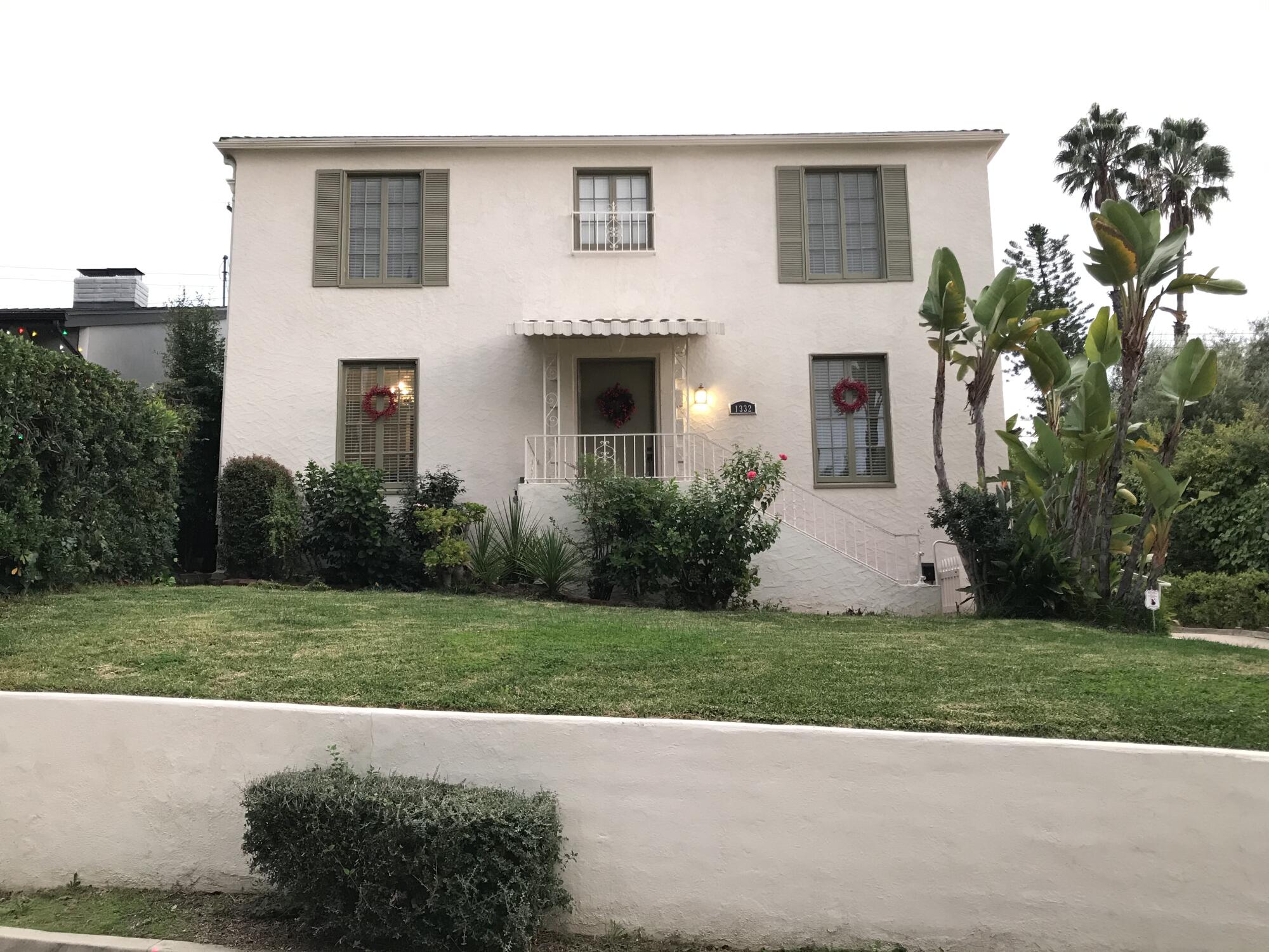 A white house with green shutters with a lawn.