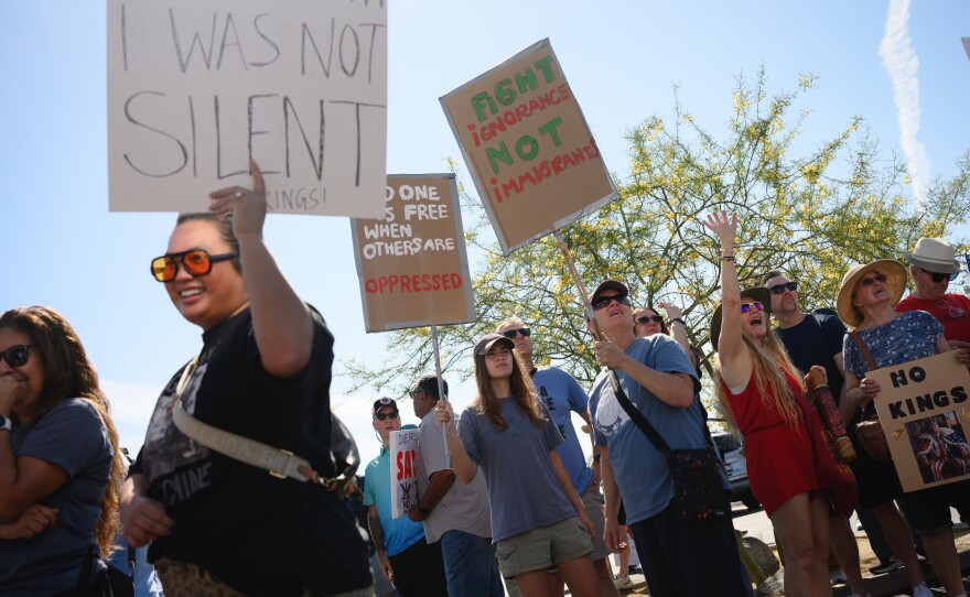 Demonstrators wave at a passing helicopter from the corner of La Mesa Boulevard and University Avenue in La Mesa, California during a nationwide day of “No Kings” protests against the Trump administration’s sweeping immigration crackdown, military strikes in Iran and other policies on March 28, 2026.