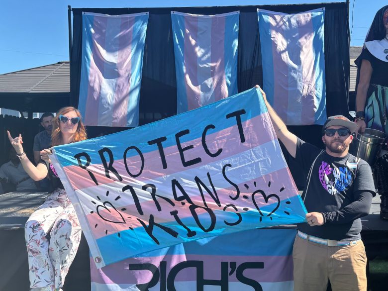 Two people hold a transgender flag with a message reading PROTECT TRANS KIDS in San Diego