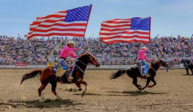two riders on horses holding U.S. flags