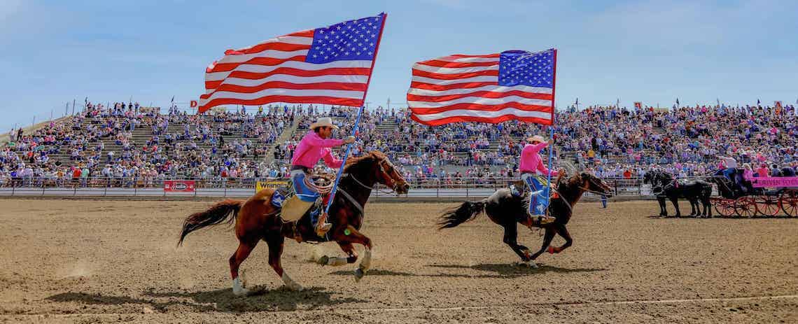 two riders on horses holding U.S. flags
