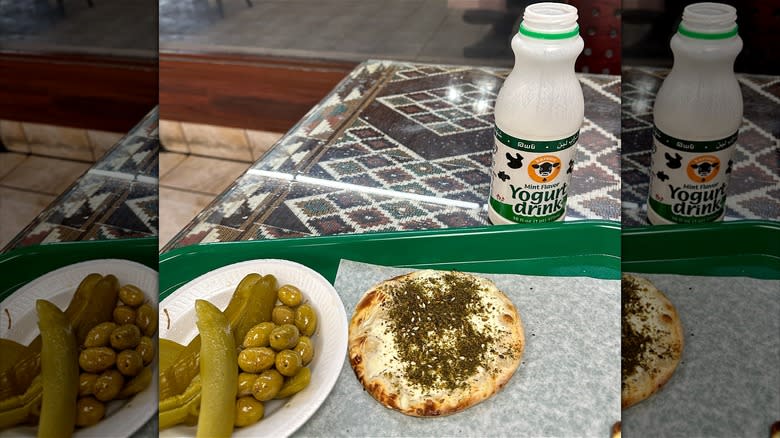 Single za'atar and cheese mana'eesh with pickles, olives, and yogurt drink.