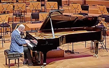Composer plays at a black grand piano on a concert stage.