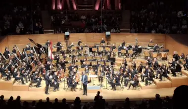 Composer plays at a black grand piano on a concert stage.