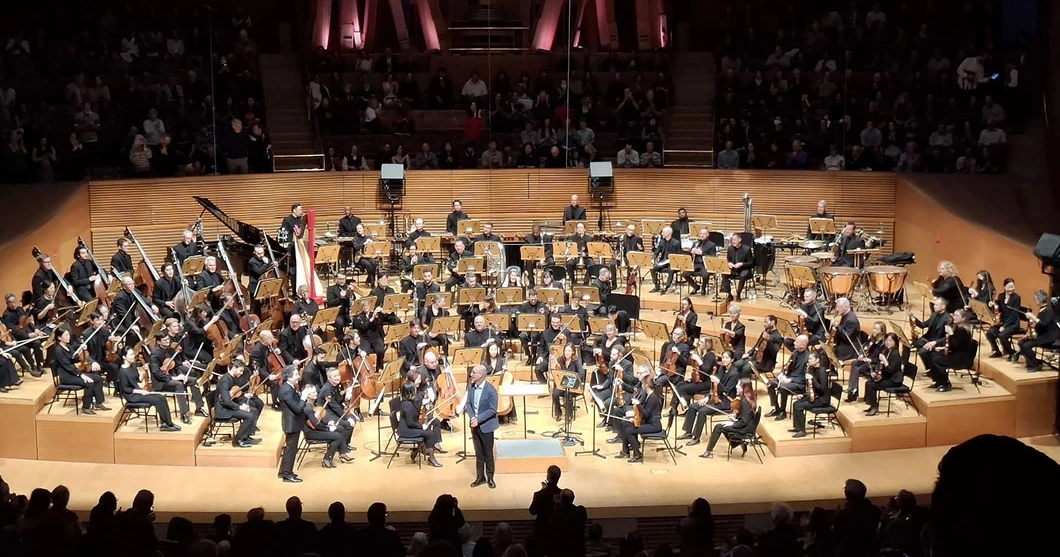 Composer plays at a black grand piano on a concert stage.