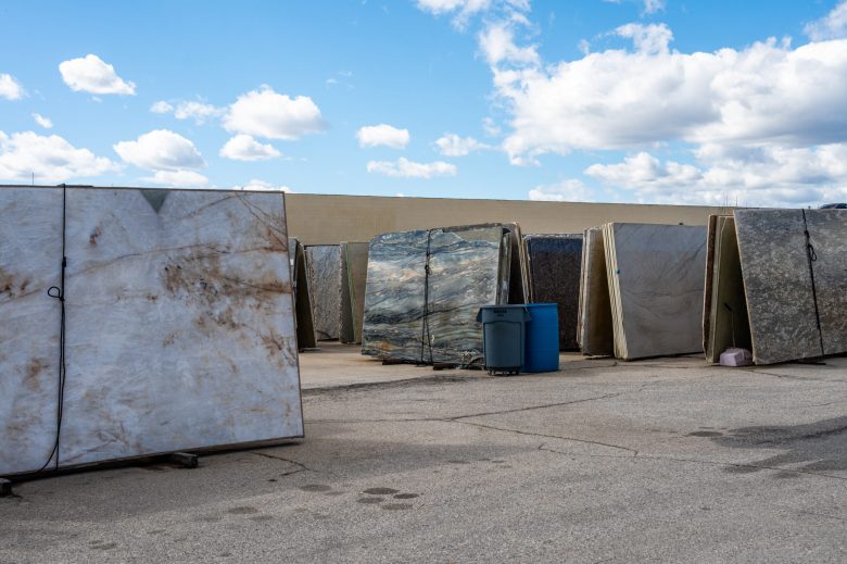 Several large stone slabs with various colors and patterns stand upright in a yard, under a mostly clear sky.