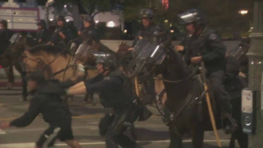 Officers detain protesters as mounted police and tactical units respond to clashes during the “No Kings” protest in downtown Los Angeles.