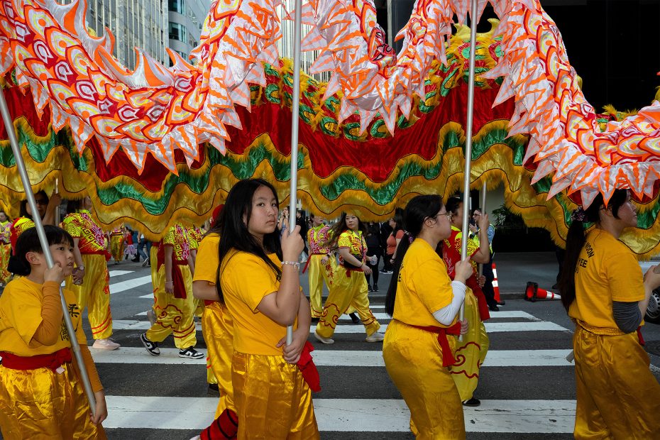 People in yellow costumes carry a colorful dragon figure during a parade on a city street, participating in a traditional cultural celebration.