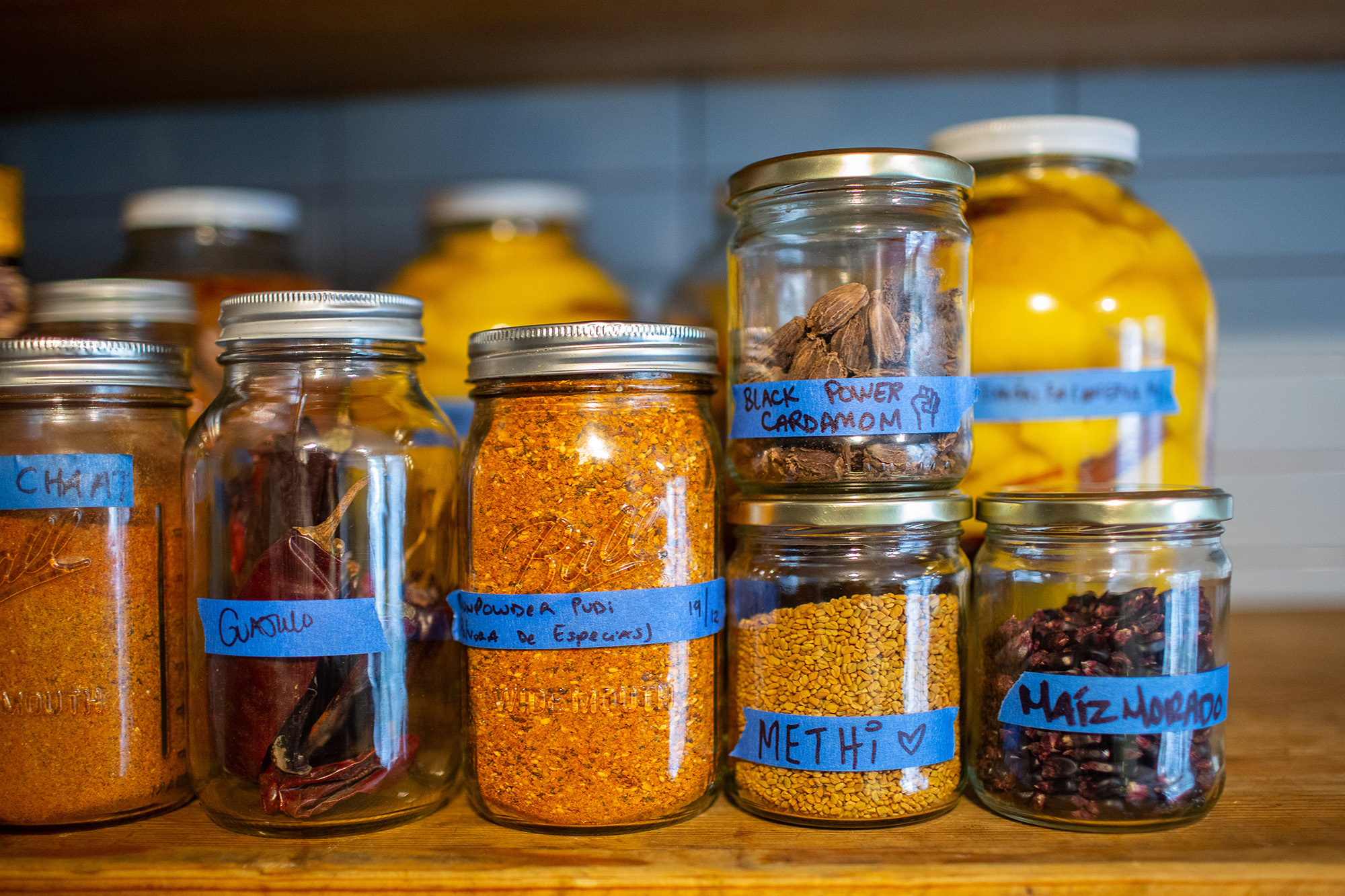 Jars of spices labeled with blue tape, including dried guajillo chiles, gunpowder pudi, 