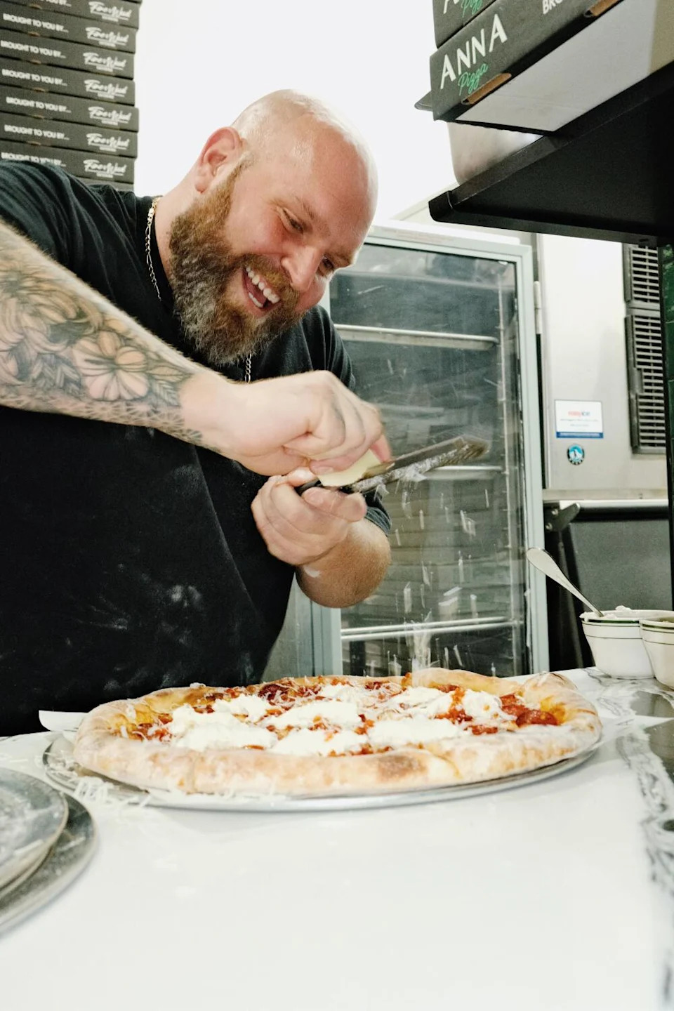 Anna Pizza chef-owner Thomas DeSantis grate cheese onto a pizza in a kitchen