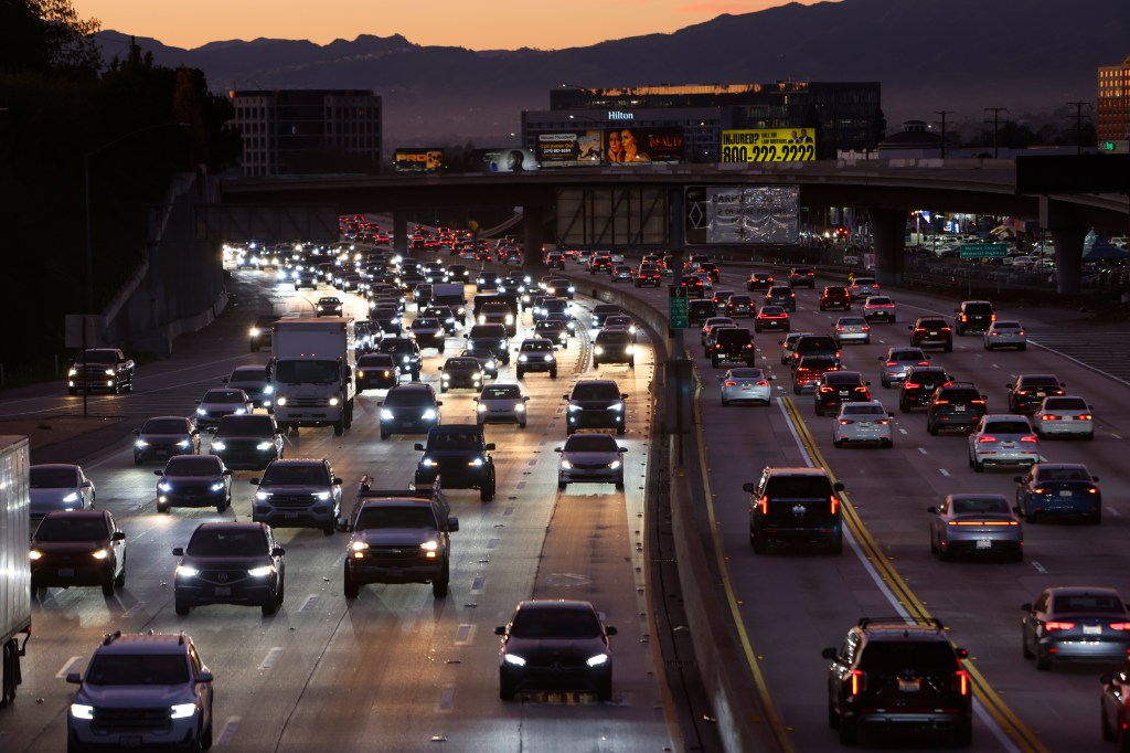 Traffic flows on Interstate 405 at sunset, with cars showing illuminated headlights and taillights.