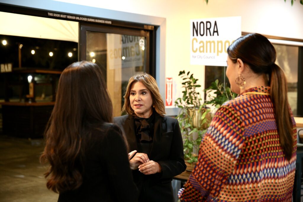 A woman facing the camera speaks to two other women with their backs to the camera