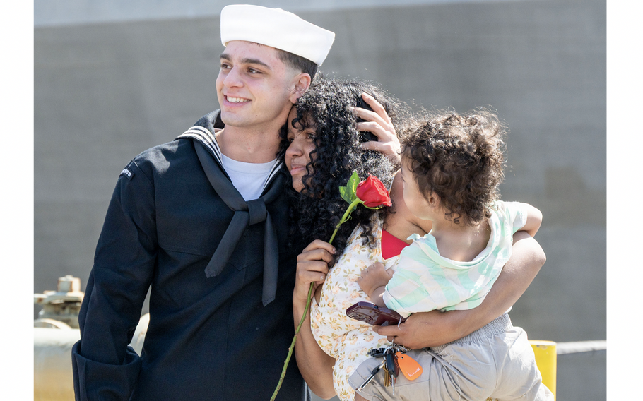 A sailor embraces a woman while she holds a child.