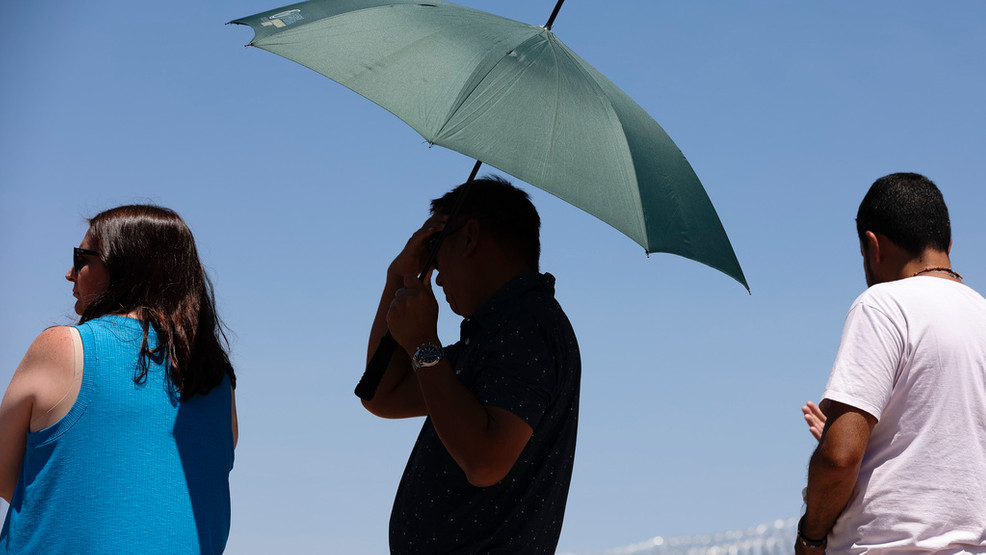 A person uses an umbrella to block the sun while waiting to take a photo at the "Welcome to Las Vegas" sign Monday, July 8, 2024, in Las Vegas. After causing deaths and shattering records in the West over the weekend, a long-running heat wave will again grip the U.S. on Monday, with hot temperatures also predicted for large parts of the East Coast and the South. (Wade Vandervort/Las Vegas Sun via AP)