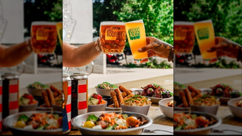 Hands toasting with glasses of beer over table of food