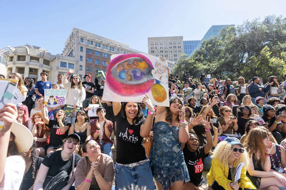 (Left to right) Daisy Johnston, 17, and Naturelle Henninger, 18, hold up a sign honoring Alysa Liu during the Alysa Liu Celebration Rally at Frank Ogawa Plaza in front of Oakland City Hall in Oakland, Calif., on March 12, 2026. (Douglas Zimmerman/SFGATE)