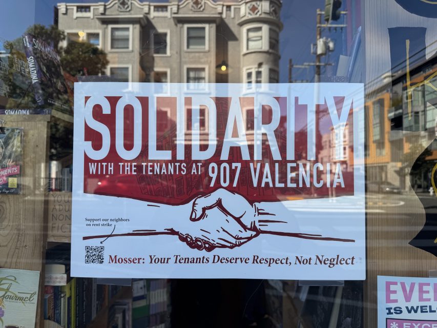 A sign in a window reads "Solidarity with the tenants at 907 Valencia" with an illustration of two hands shaking and a message about tenant respect and neglect.