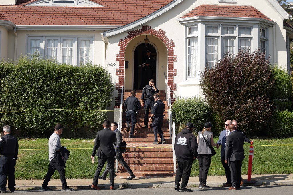 Police officers and other personnel are gathered around the entrance of a house, marked off with yellow tape, where four people were found dead in San Francisco.