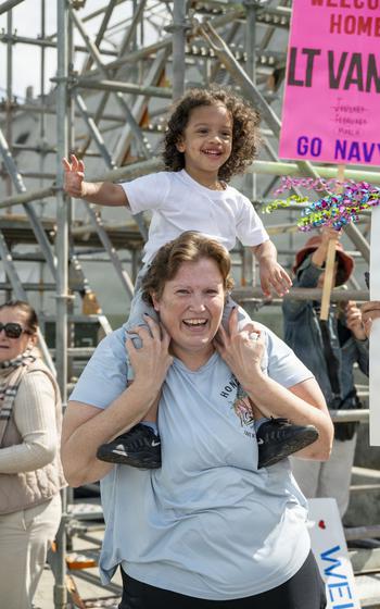 A child smiles while sitting on the shoulders of a woman.
