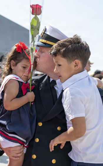 A sailor carries two children and kisses the head of a young girl.