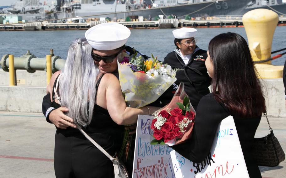 A sailor hugs a woman with flowers and poster boards.