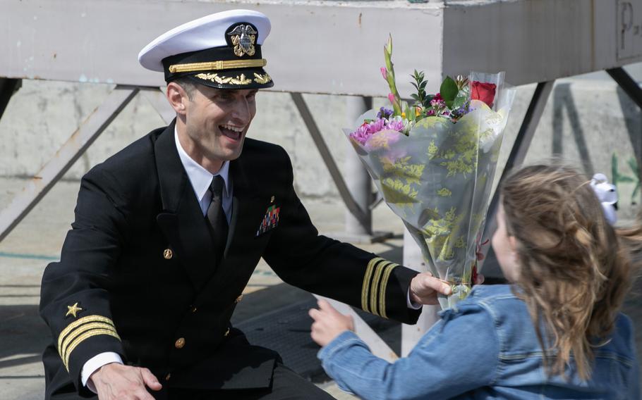 A sailor smiles and opens his arms as a girl runs toward him.