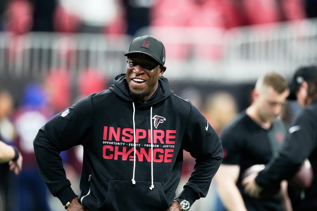 Atlanta Falcons coach with a wide smile, wearing a black hoodie and a black cap with the Falcons logo.