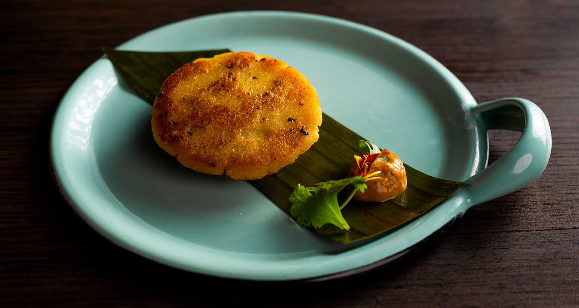 Beautifully plated arepa, served on top of a banana leaf with a delicate dollop of orange sauce.