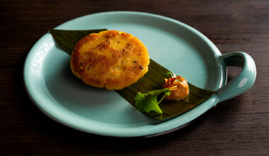 Beautifully plated arepa, served on top of a banana leaf with a delicate dollop of orange sauce.
