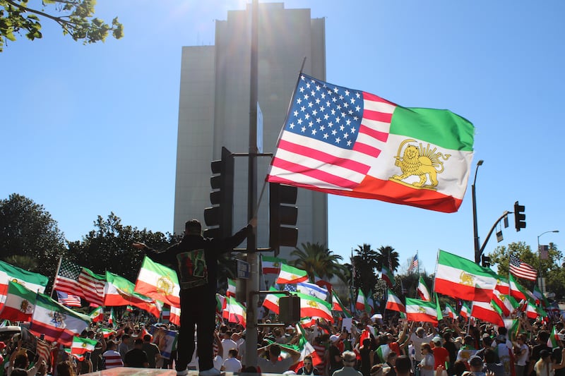 A participant stands on a ledge across from the Wilshire Federal Building in Westwood, waving a flag and joining the crowd in chants. (Photo by Charlotte Calmès)