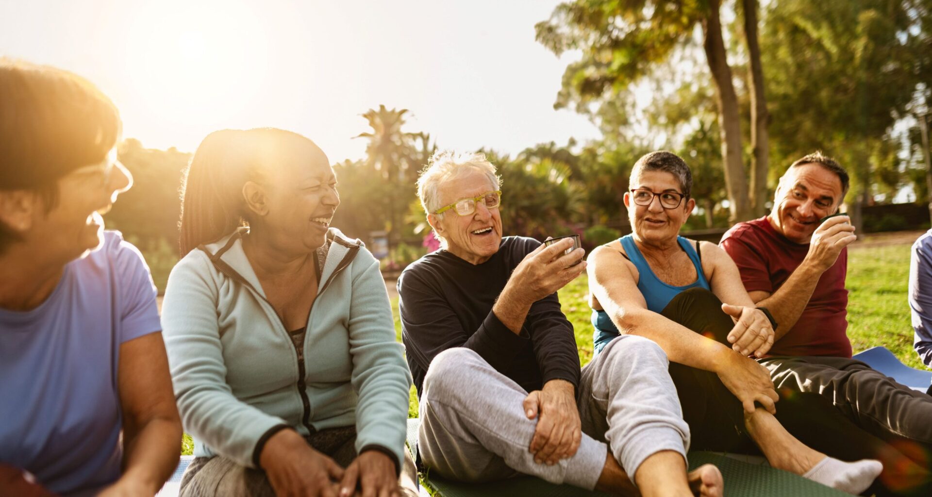 Diverse group of seniors sitting outdoors, drinking tea after exercising