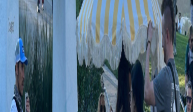 A chocolate-covered banana on a stick is drizzled with peanut butter and sprinkled with crushed nuts, held in a small brown paper tray.