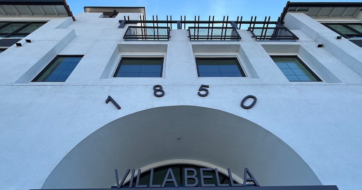 A white building with black-framed windows features the number "1850" above an archway labeled "VILLABELLA" in metal letters.