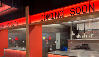 Two empty, modern service counters with red tiled fronts and stainless steel surfaces display "COMING SOON" in black letters on bright red backlit signs above.