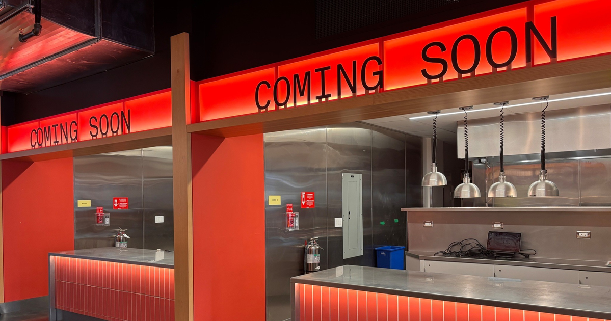 Two empty, modern service counters with red tiled fronts and stainless steel surfaces display "COMING SOON" in black letters on bright red backlit signs above.
