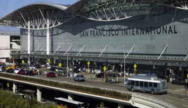 San Francisco International Airport’s main terminal with multiple lanes of traffic, buses, cars, and a clear blue sky overhead.