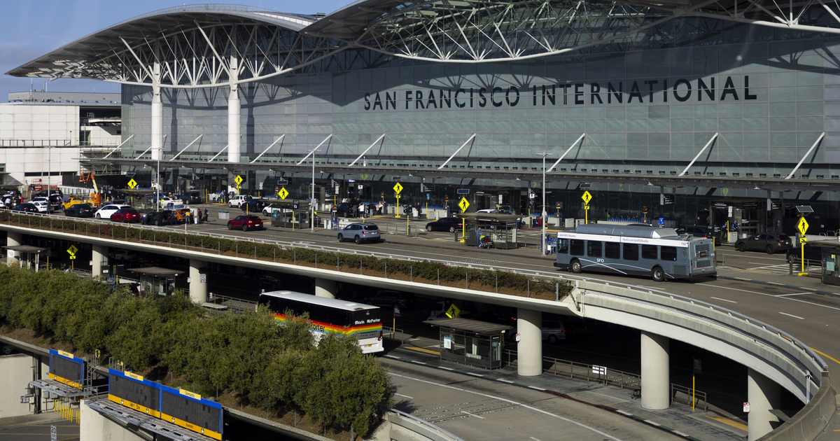 San Francisco International Airport’s main terminal with multiple lanes of traffic, buses, cars, and a clear blue sky overhead.