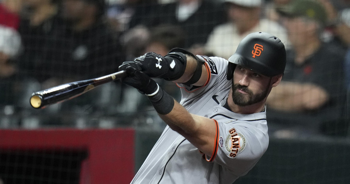 A baseball player wearing a San Francisco Giants uniform swings a bat during a game, focusing intently on the ball.