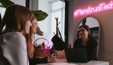 A syringe filled with red liquid stands upright in a small, round plastic container partially filled with the same red liquid.