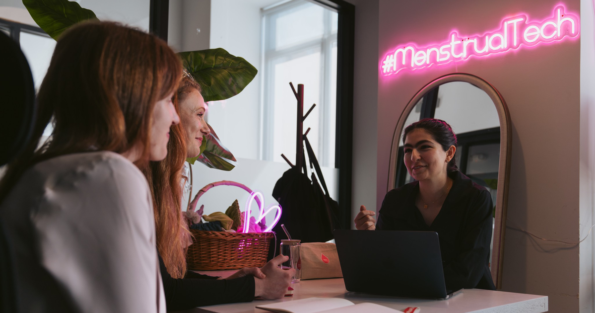 A syringe filled with red liquid stands upright in a small, round plastic container partially filled with the same red liquid.