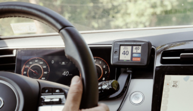 A hand grips a Hyundai steering wheel, the car speed shows 40 mph, a GPS displays a maximum speed of 40 mph, and a push-start button is visible.